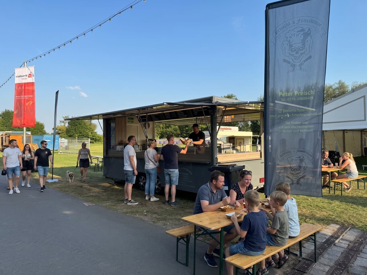 Foodtruck bei einem Sommerfest, Familie mit Kindern am Biertisch bei blauem Himmel