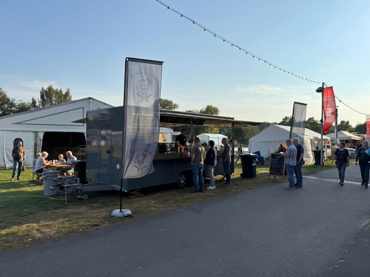 Foodtruck am Seeufer bei einem Festival in der Abendsonne, Gäste in der Warteschlange
